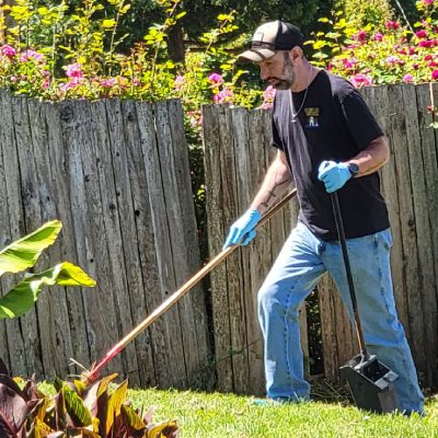 A man is actively raking leaves in a yard, working to maintain a clean and organized outdoor environment